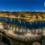 Night view of Lake Park Riyadh with lit lake, palm trees, and city lights.