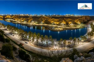 Night view of Lake Park Riyadh with lit lake, palm trees, and city lights.