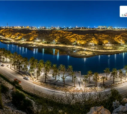 Night view of Lake Park Riyadh with lit lake, palm trees, and city lights.