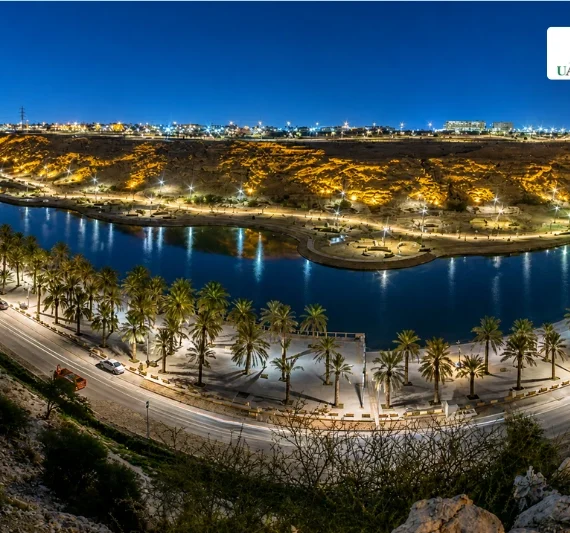Night view of Lake Park Riyadh with lit lake, palm trees, and city lights.